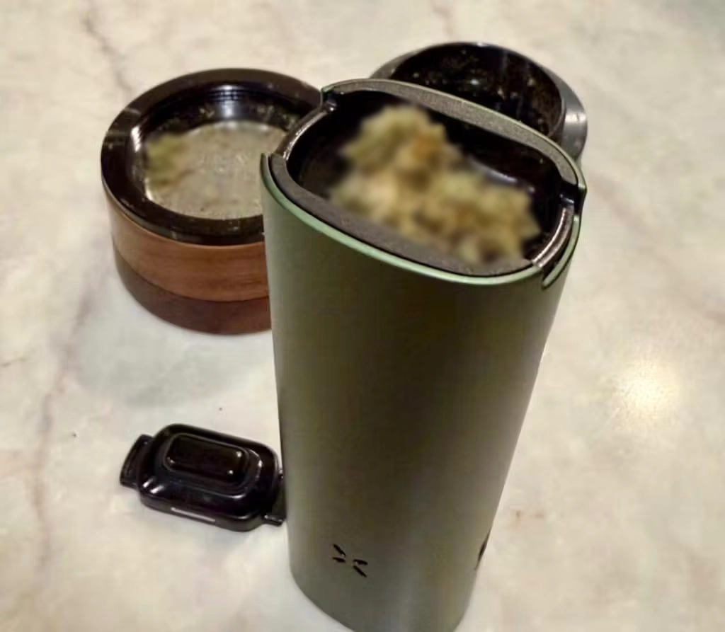 A customer's Greenstone PAX FOUR packed with ground flower beside a wood grinder on a marble counter